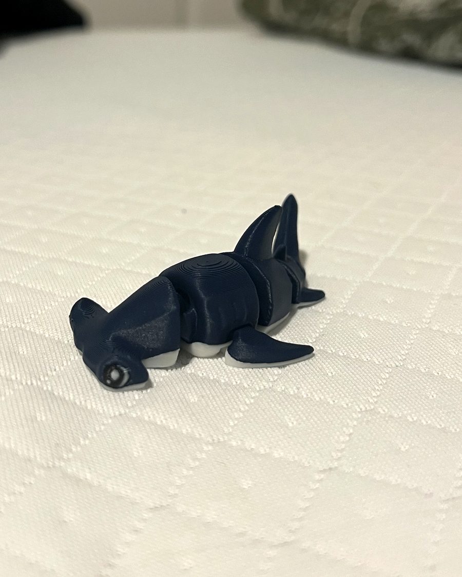 A navy blue hammerhead shark figure resting on a white bed.