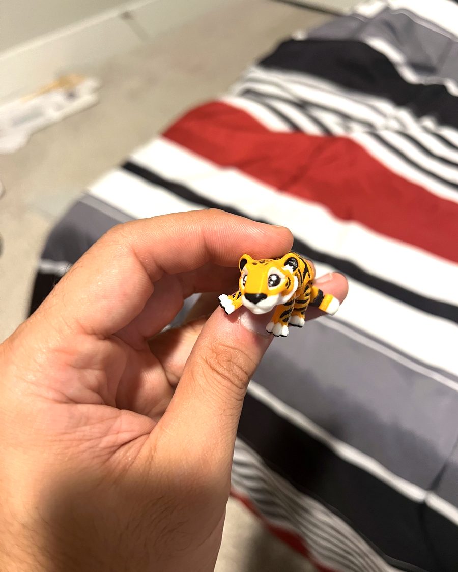 A tiny orange and black tiger figure held between finger and thumb, a striped blanket behind it.